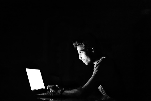A man working with his laptop, in the dark.